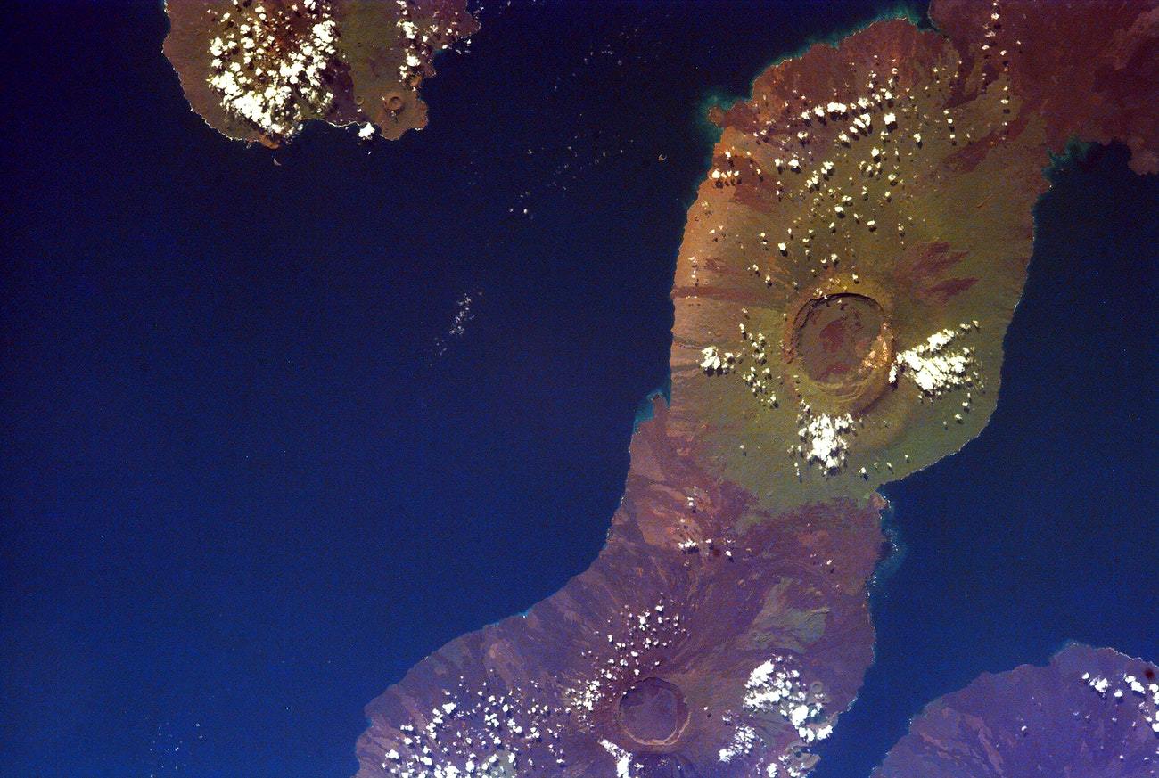 A NASA photograph featuring the Galapagos Islands viewed from space, with a blend of blue and purple hues representing different terrains.