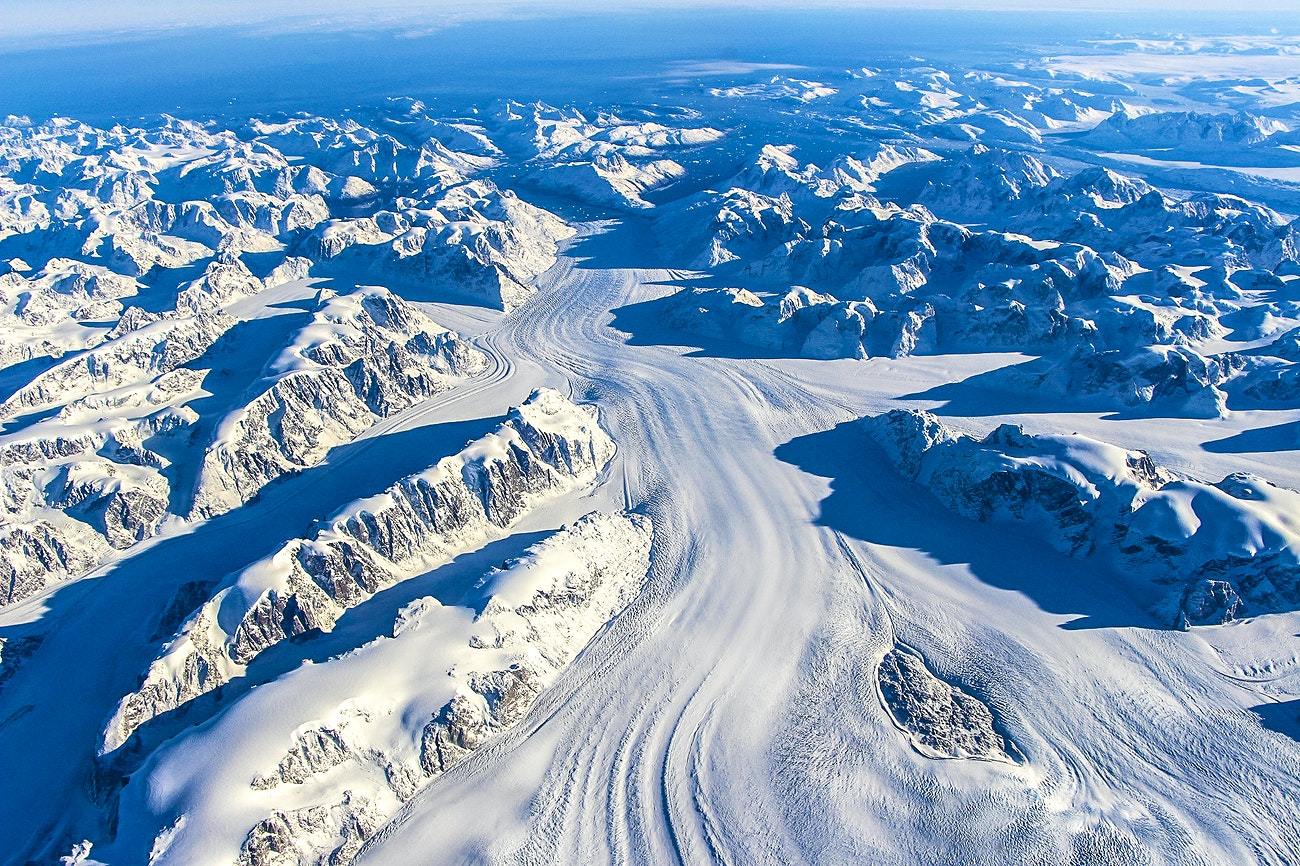 Aerial view of a glacier in southern Greenland, showcasing white ice and snow-covered landscapes with blue skies.