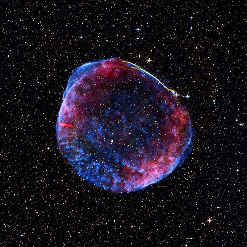 A colorful image of a planetary nebula in space, featuring shades of pink, blue, and red against a black background speckled with stars.
