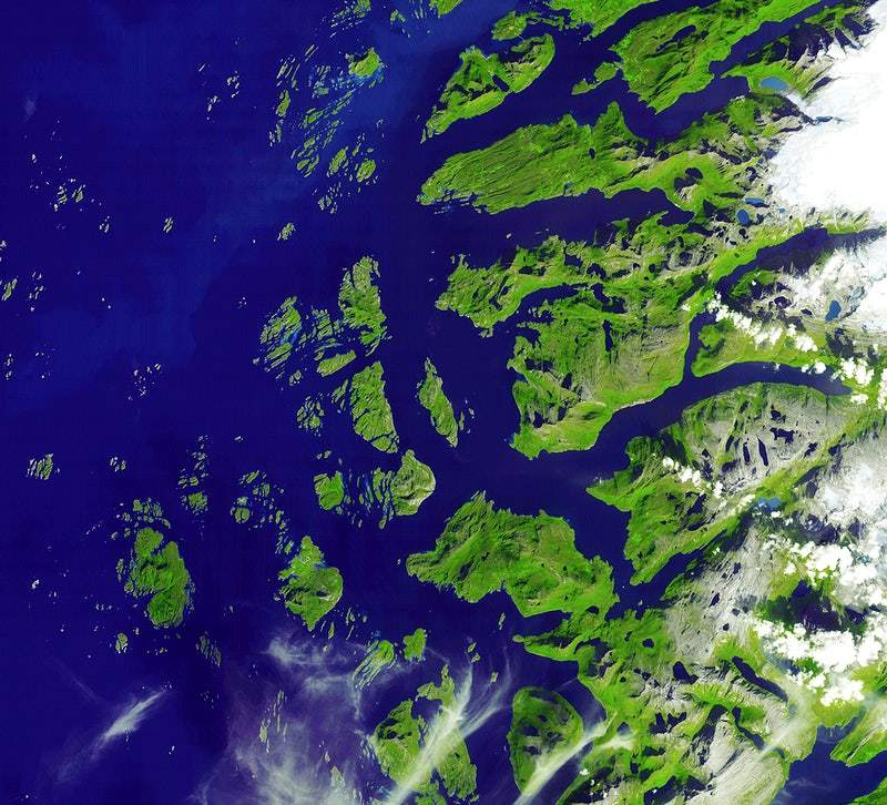 A satellite image of the Arctic Circle showing green landmasses and blue waters, with some cloud formations.