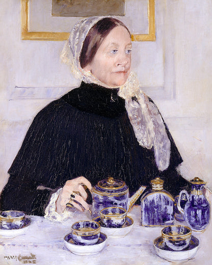 Woman sitting at a table with a tea set, wearing a black dress and white lace headscarf.