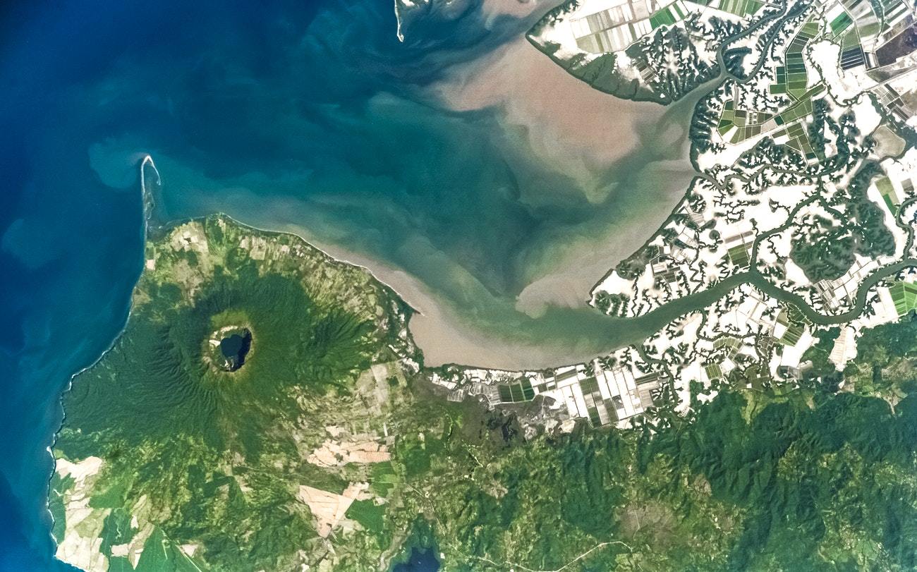 A panoramic photo of a volcanic landscape on Earth, likely the Cosiguina Volcano, viewed from a high altitude or space with surrounding greenery and bodies of water.