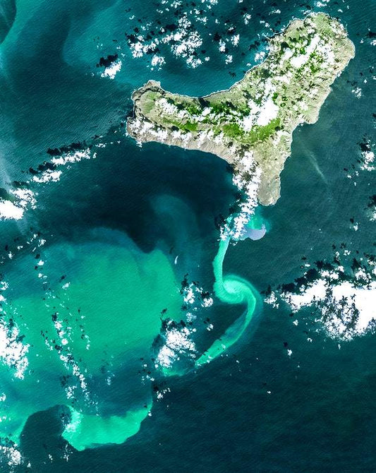 A satellite image of an underwater volcanic eruption, showing a vivid turquoise plume against darker water.